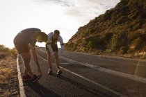 Vista lateral do pai e do filho caucasianos fazendo exercício de alongamento na estrada pela manhã — Fotografia de Stock