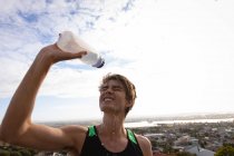 Front view of young Caucasian man pouring water on his face on a sunny day — Stock Photo