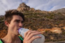 Primer plano de un joven caucásico bebiendo agua en el campo - foto de stock