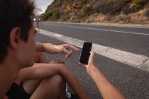 Через плечо вид отца и сына глядя на мобильный телефон во время отдыха на дороге — стоковое фото