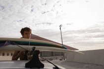 Vue de face du jeune homme caucasien debout avec planche de surf à la plage — Photo de stock