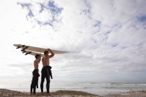 Tiefansicht von kaukasischem Vater und Sohn, die mit Surfbrett am Strand stehen — Stockfoto