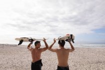 Vue arrière du père et du fils caucasiens debout avec planche de surf à la plage — Photo de stock