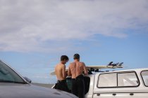 Vista trasera de padre e hijo caucásicos de pie cerca de coche en la playa - foto de stock