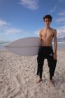 Portrait of Caucasian young man standing with surfboard at beach — Stock Photo