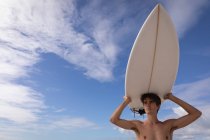 Низький кут зору молодий Кавказький чоловік, що стоять з дошки для серфінгу на пляжі в сонячний день — стокове фото