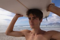 Primo piano del giovane caucasico in piedi con la tavola da surf in spiaggia in una giornata di sole — Foto stock
