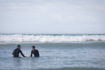 Vue de face de père caucasien insouciant et fils surf avec planche de surf dans la mer — Photo de stock