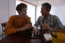 Vista frontal de padre e hijo caucásicos interactúan mientras toman cerveza en casa - foto de stock