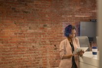 Vista frontal de la mujer de negocios afroamericana utilizando tableta digital contra la pared de ladrillo en la oficina - foto de stock