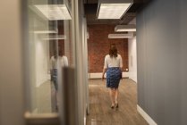 Задній вид кавказької ділової жінки, що йде в офісному коридорі — стокове фото