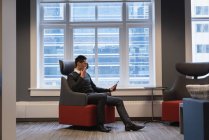 Вид сбоку на азиатского бизнесмена, использующего цифровой планшет во время разговора по мобильному телефону в офисе — стоковое фото