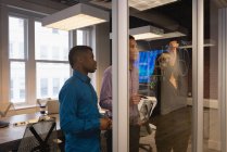 Vue latérale de divers hommes d'affaires projetant sur un mur de verre dans la salle de conférence au bureau — Photo de stock