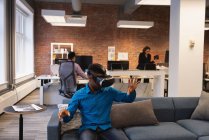 Front view of African-american businessman using virtual reality headset while colleagues working in background at office — Stock Photo