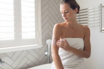Красива жінка наносить лосьйон на її тіло у ванній вдома — стокове фото