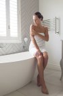 Hermosa mujer que aplica loción en su cuerpo en el baño en casa - foto de stock