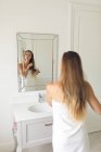 Зеркальный образ красивой женщины расчесывать волосы в ванной комнате дома — стоковое фото