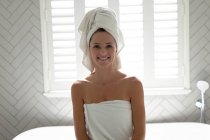 Портрет усміхненої жінки, що сидить на краю ванни у ванній — стокове фото