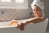 Donna sorridente seduta nella vasca da bagno in bagno a casa — Foto stock
