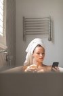 Красивая женщина пьет шампанское и проверяет телефон в ванной дома — стоковое фото