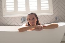 Портрет улыбающейся женщины, опирающейся на ванну в ванной комнате — стоковое фото