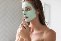 Primer plano de la mujer reflexiva con máscara facial sentado en el baño - foto de stock