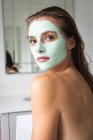 Крупным планом красивая женщина в маске для лица сидит в ванной комнате — стоковое фото