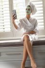Mulher bonita em roupão de banho tirar uma selfie em casa — Fotografia de Stock