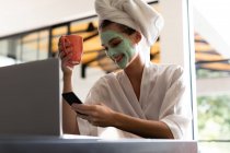 Sorrindo mulher em roupão de banho verificando seu telefone enquanto toma café — Fotografia de Stock
