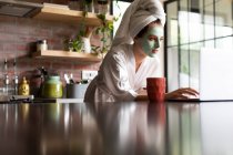 Schöne Frau im Bademantel mit Laptop auf dem Küchentisch zu Hause — Stockfoto
