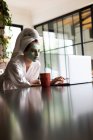 Beautiful woman in bathrobe using laptop on the kitchen counter at home — Stock Photo