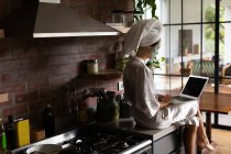Женщина в халате сидит на кухонном столе и пользуется ноутбуком по утрам — стоковое фото