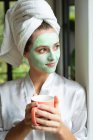 Frontansicht einer Frau mit Gesichtsmaske mit Kaffeebecher zu Hause — Stockfoto