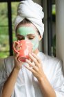 Вид спереду жінки в масці для обличчя п'є каву вдома — стокове фото