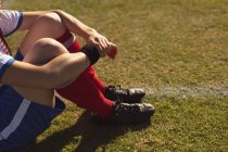 Mid section of female soccer player sitting at sports field on a sunny day — Stock Photo