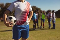 Серединна секція кавказької жіночої футболіста з м'ячем стоячи на спортивному полі в сонячний день — стокове фото