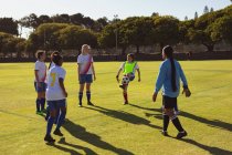 Visão traseira de diversas jogadoras de futebol jogando futebol no campo esportivo em um dia ensolarado — Fotografia de Stock