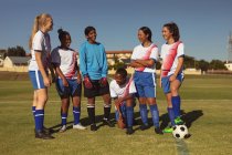 Vista frontal de diversas jogadoras de futebol discutindo estratégia no campo esportivo em um dia ensolarado — Fotografia de Stock
