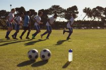 Vista lateral de diversas jogadoras de futebol que correm em uma linha no campo esportivo em um dia ensolarado . — Fotografia de Stock