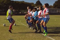 Vue latérale de diverses joueuses de soccer s'échauffant sur un terrain de sport par une journée ensoleillée — Photo de stock