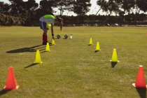 Vista lateral de una futbolista caucásica arreglando conos en el campo para practicar en un día soleado - foto de stock