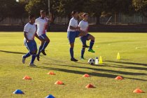 Vue latérale de diverses joueuses de soccer faisant de l'exercice d'échauffement sur le terrain par une journée ensoleillée — Photo de stock