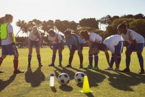 Vue de face de l'entraîneur féminin caucasien aidant diverses joueuses de soccer avec l'exercice d'échauffement sur le terrain de sport — Photo de stock