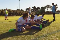 Vista lateral de diversas jogadoras de futebol fazendo exercícios de alongamento em campo em um dia ensolarado — Fotografia de Stock