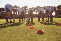 Vista frontal de diversas jogadoras de futebol fazendo exercício de aquecimento no campo em um dia ensolarado — Fotografia de Stock