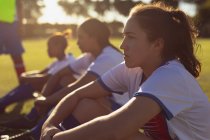 Seitenansicht entschlossener unterschiedlicher Fußballerinnen, die an einem sonnigen Tag auf dem Sportplatz sitzen — Stockfoto