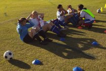 High angle view of diverse female soccer players doing crunches at the sports field on a sunny day — Stock Photo
