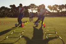 Vorderansicht diverser Fußballerinnen, die während des Trainings auf dem Feld den Ball zwischen den Kegeln vorbeischieben — Stockfoto