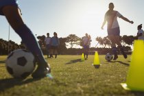 Vue en angle bas de diverses joueuses de soccer passant le ballon entre les cônes pendant l'entraînement sur le terrain — Photo de stock