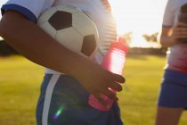 Средняя часть футболистки держит мяч и бутылку воды на поле — стоковое фото